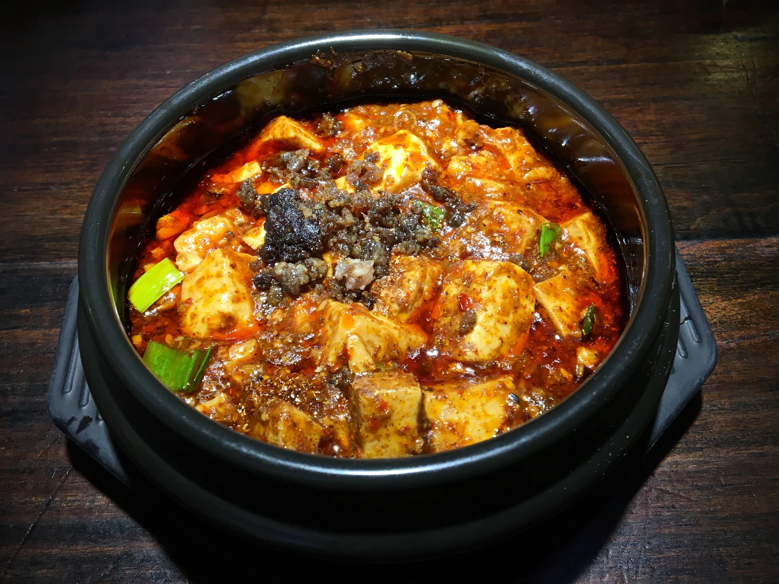 Mapo tofu topped with Sichuan pepper and red chili oil in a dark serving bowl