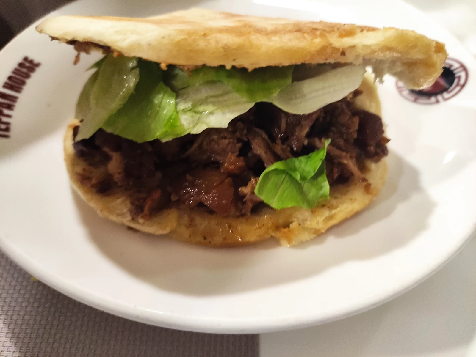 A roujiamo filled with braised meat and herbs on a white plate