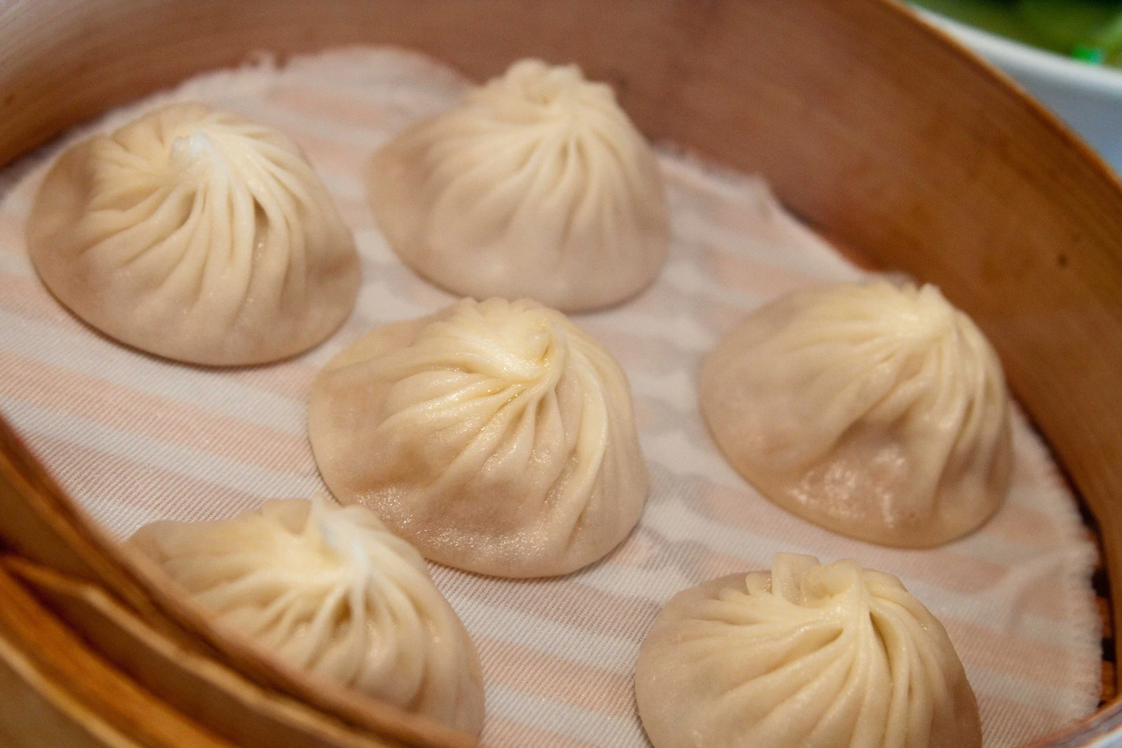 Delicately pleated xiaolongbao soup dumplings in a bamboo steamer