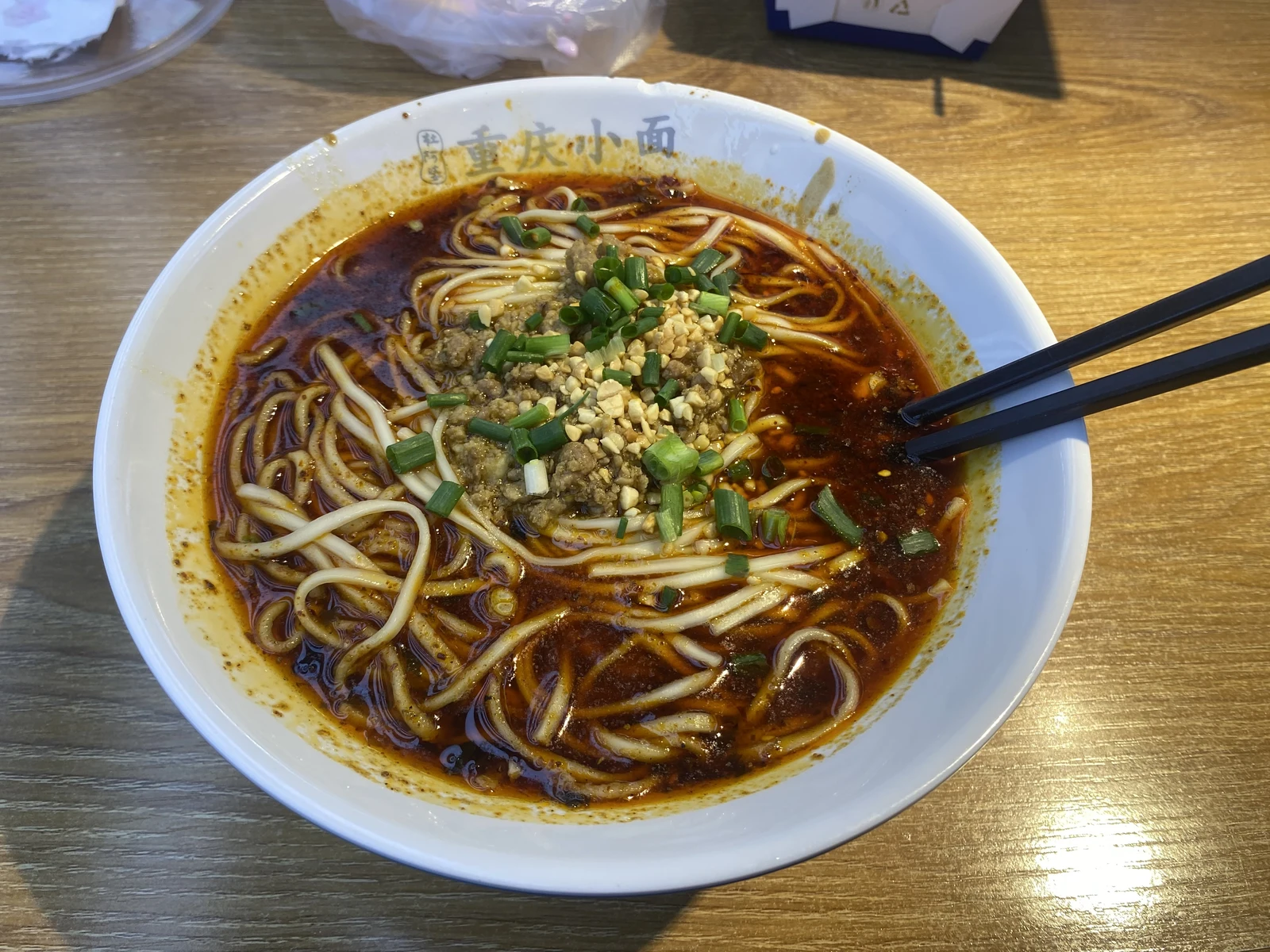 A bowl of Chongqing-style spicy noodles topped with peanuts and spring onion