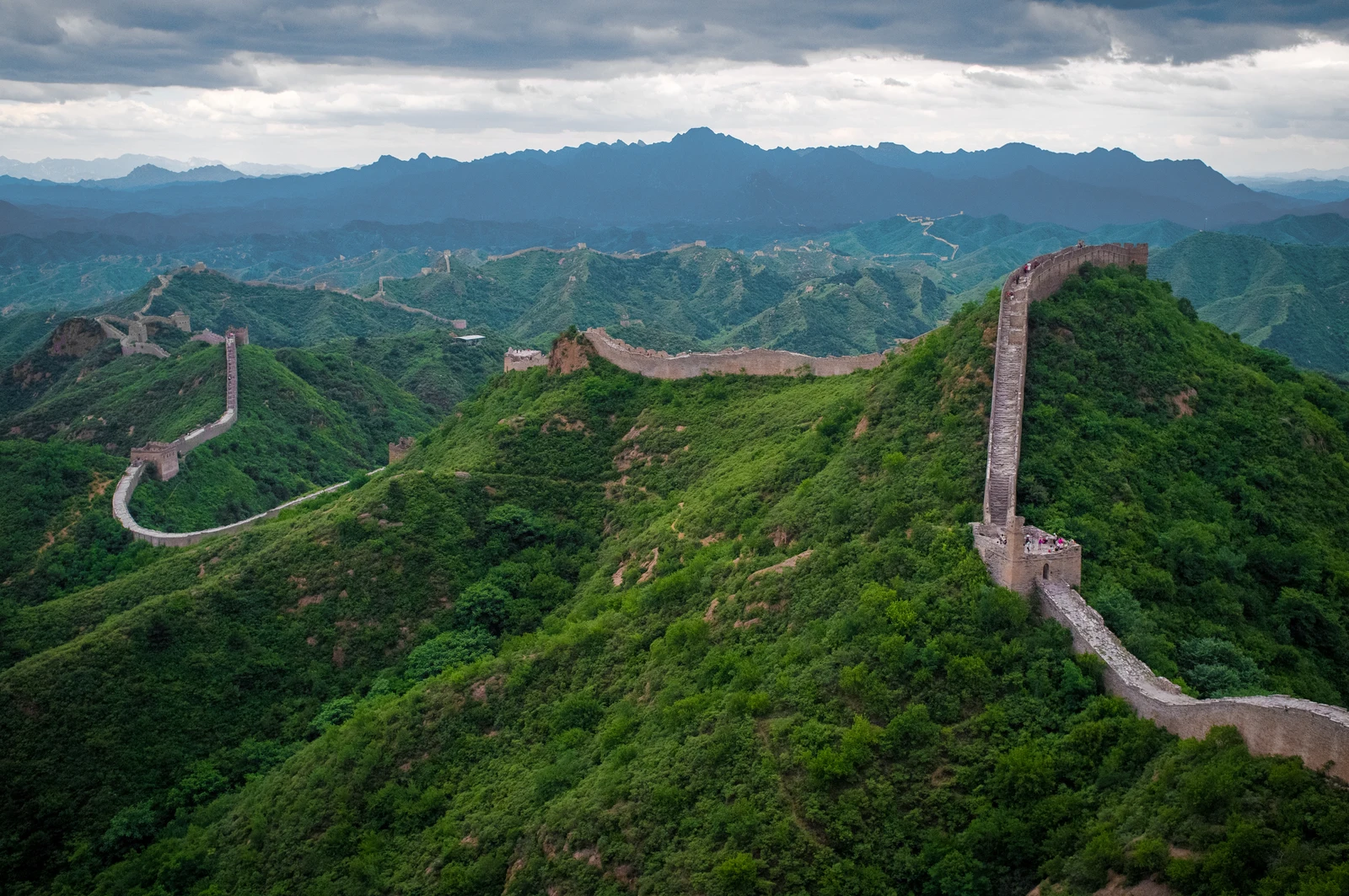 The Great Wall winds across green mountain ridges at Jinshanling beneath dramatic clouds