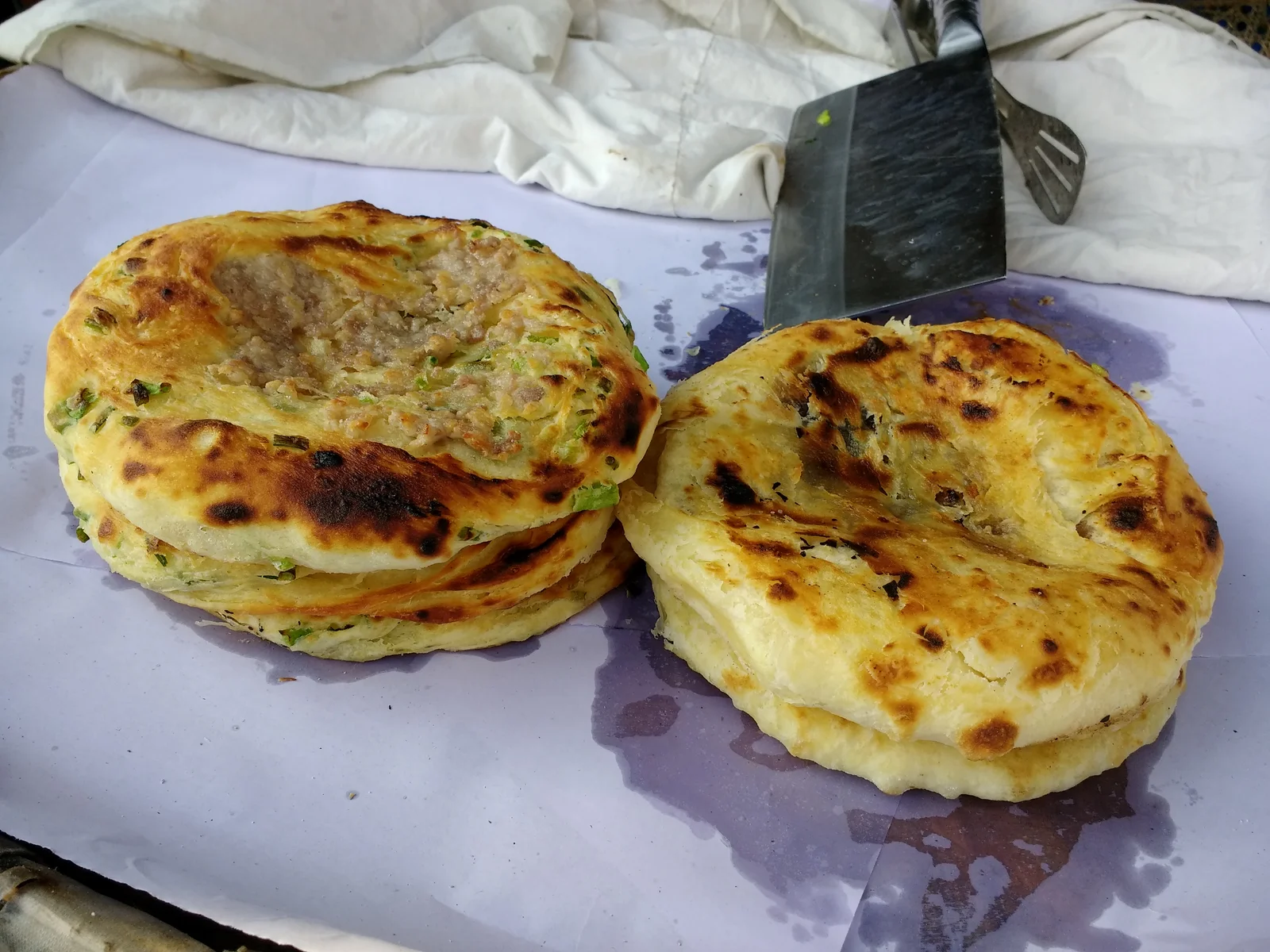Two golden Xizhou baba meat-filled flatbreads on a street-food counter
